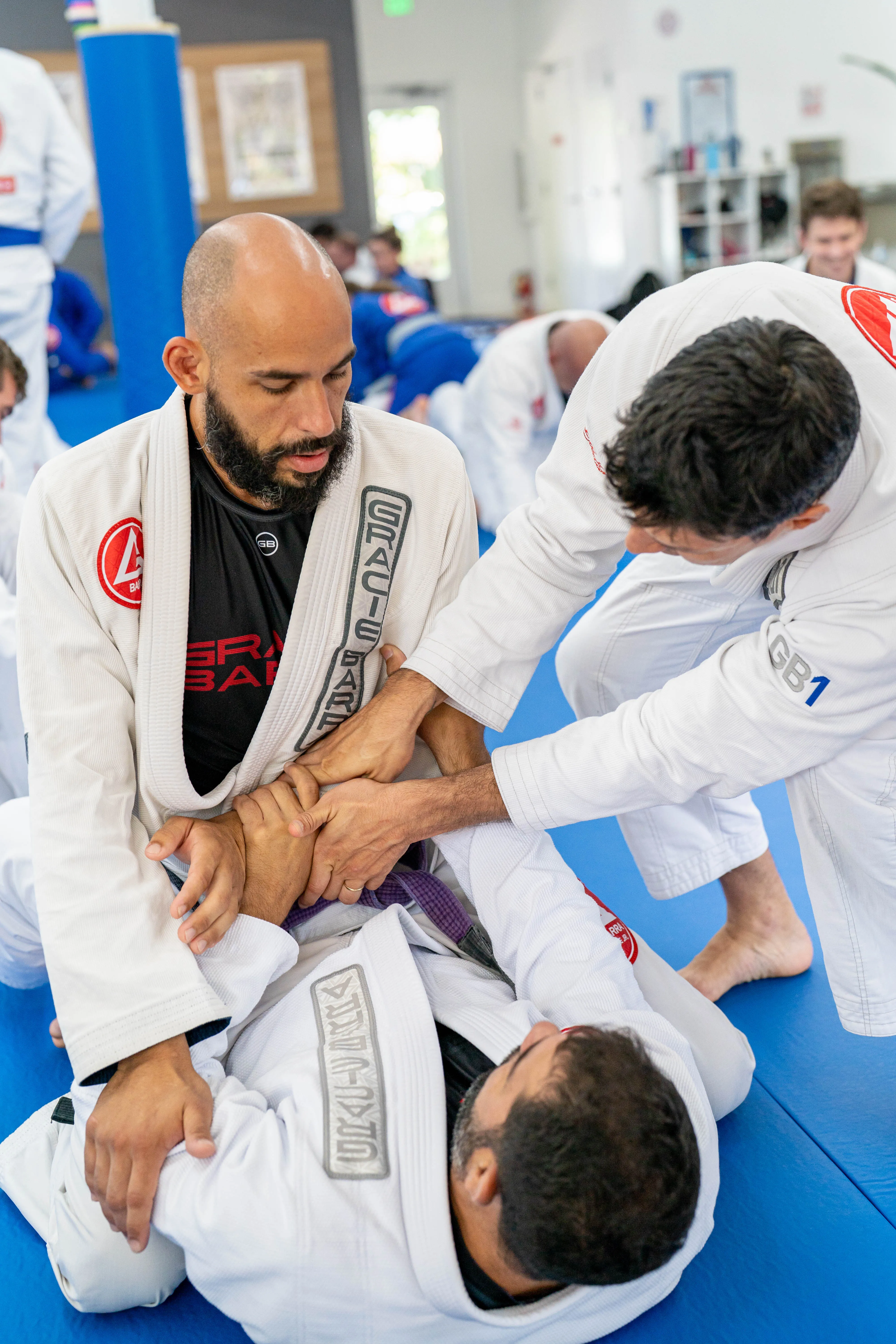An instructor works through a grappling technique with two adult students during class.